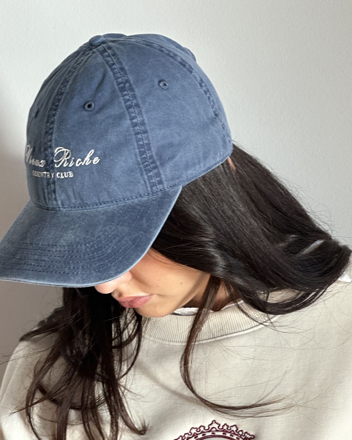 Woman wearing Vieux Riche Country Club Classic cap in vintage blue, with a sweatshirt visible underneath.