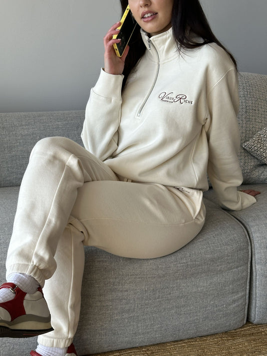 Woman wearing Vieux Riche Heritage Club track pants in ivory with a matching half-zip sweatshirt, talking on the phone.