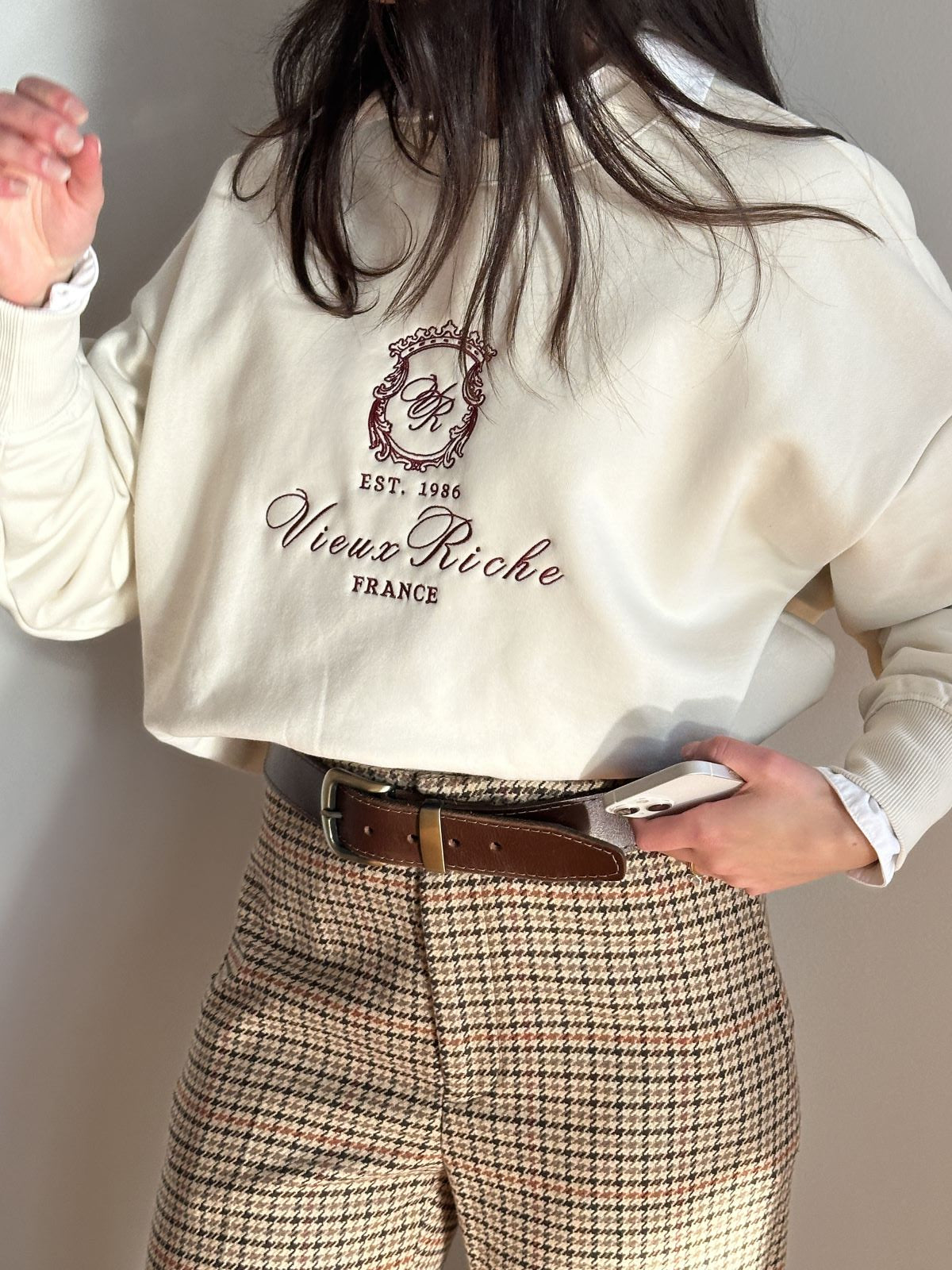 Woman wearing Vieux Riche Legacy Luxe crew neck sweatshirt in ivory red with woollen old money Ralph Lauren trousers.