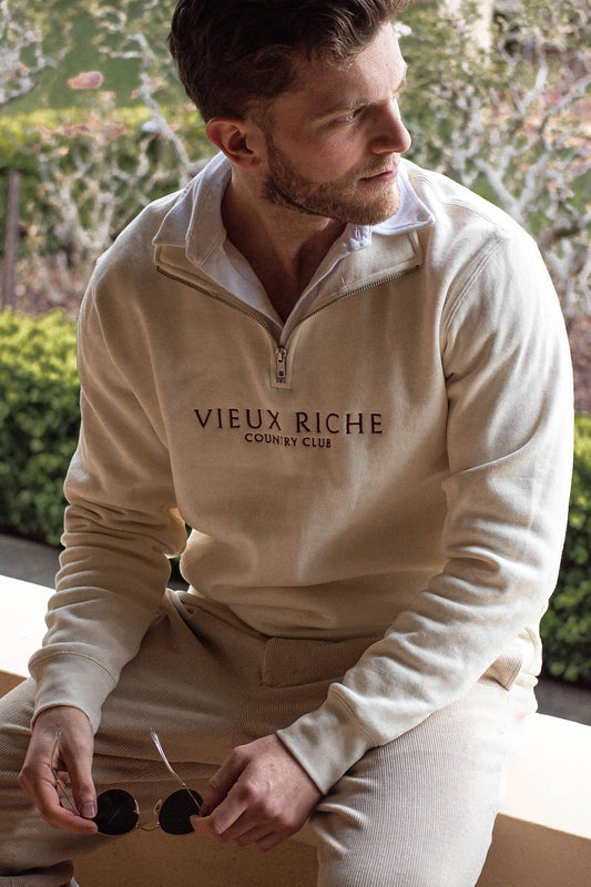 Man showcasing vintage charm on veranda with sunglasses and Ivory Clubhouse Classic Half Zip.