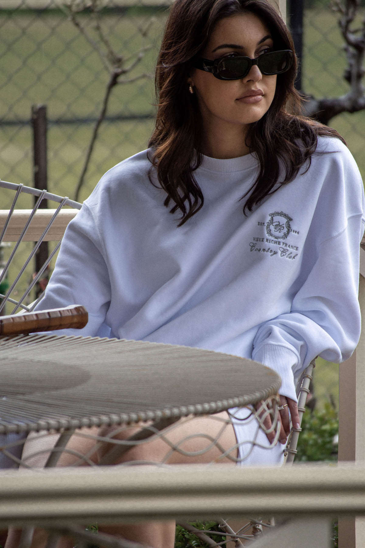 Woman with sunglasses sitting gracefully in the Court Couture Blanc Crew, channelling white old money fashion.